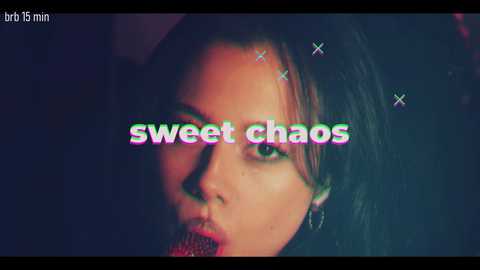 A close-up video of a woman with a serious expression, wearing red lipstick, with the words \"sweet chaos\" overlaid in neon green and pink.