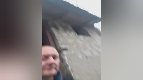 Video of a partially obscured man with fair skin, short brown hair, and a light beard, standing beside a partially collapsed concrete wall with a greyish hue, suggesting a construction site or natural disaster aftermath.