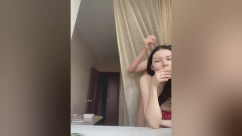 A video of a young woman with fair skin, long black hair, and a red top, captured mid-motion as she adjusts her hair in front of a bathroom mirror.