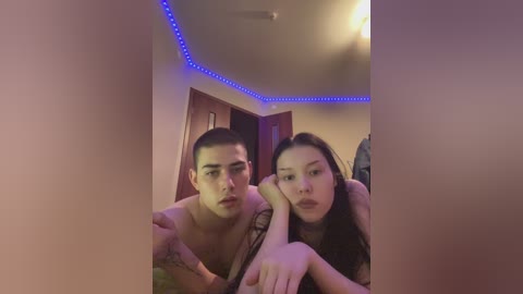 Video of two Asian men with short hair and light skin, one shirtless, hugging a woman with long black hair, in a dimly lit room with blue LED strip lights on the ceiling.