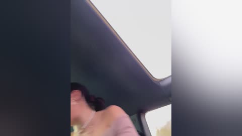 A video showing a woman with dark hair, wearing a white shirt, leaning inside a car's sunroof. The car's interior is dark, and the sky is visible through the sunroof, suggesting an open-top vehicle.