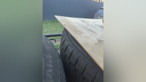 Video of a wooden table with a rough surface placed on top of two stacked tires in an outdoor setting, surrounded by green grass and a dark blue wall.