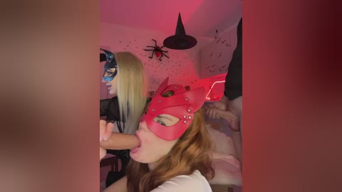 Video of two women in Halloween costumes, one with a red mask, performing oral sex on a man, in a dimly lit room with spider decorations.