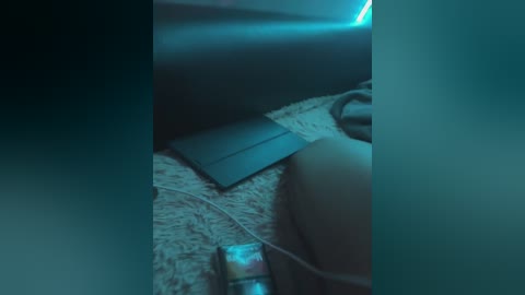 A dimly lit, grainy video of a dark room featuring a laptop, cables, and a furry rug, with a glowing blue light in the background.