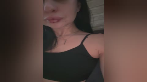 Video of a woman with fair skin and dark hair, wearing a black spaghetti strap top, taken from a low angle, with a blurry background.