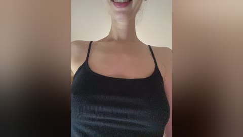 Video of a light-skinned woman with a slender build, wearing a black, ribbed tank top, her face partially visible with a slight smile.