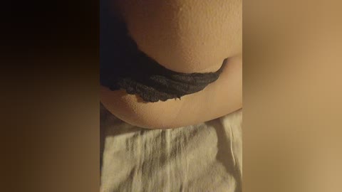 A close-up video of a woman's lower torso, showing her skin, black lace underwear, and a beige towel. The image is dimly lit, emphasizing texture and shadows.