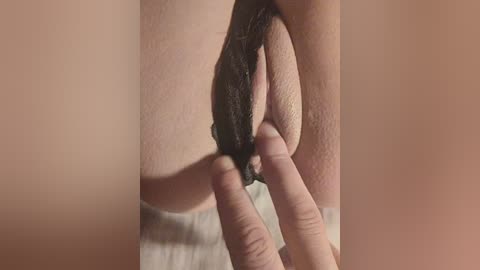 A close-up video of a person's hand pulling back the labia, revealing the vulva. The skin is light, the labia are dark, and the background is blurred.