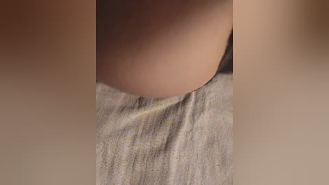 Close-up video of a light-skinned person's bare buttocks and lower back, covered in a soft, beige towel with subtle yellow stripes. The skin is smooth, with a slight blush, and the lighting is soft and natural, highlighting the texture of the fabric and skin.