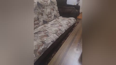 A video of a beige sofa with a patterned fabric and a wooden floor, set against a plain beige wall.
