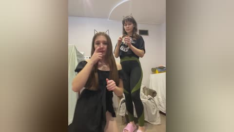 Video of two young women in cat costumes, one sitting, one standing, in a messy room with clothes on the floor.