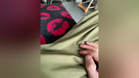 A video of a person's hand adjusting a beige garment with a black floral pattern, featuring red poppies, and a blurred background with a grey chair.