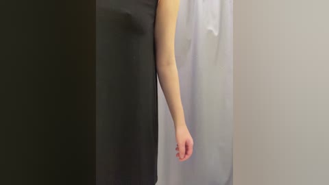 A video showing a woman's arm in a sleeveless black dress, with a white curtain behind her, indicating a bathroom setting. Her arm is relaxed and the focus is on the fabric texture and contrast.