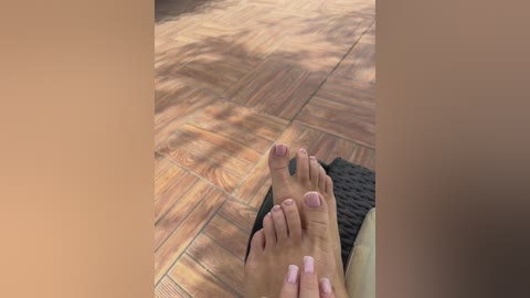 Video of a person's feet with neatly trimmed nails and light pink polish, resting on a warm-toned, patterned tile floor, with a woven black mat visible in the background.
