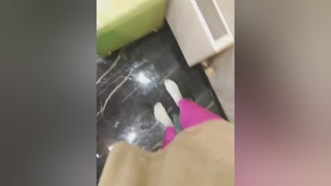 A video showing a person in a black hoodie and pink gloves, standing on a dark, reflective surface, with blurred background objects.