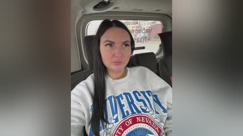 Video of a woman with long black hair wearing a grey \"Chicago of Nevada\" sweatshirt, seated in a car, looking contemplative.
