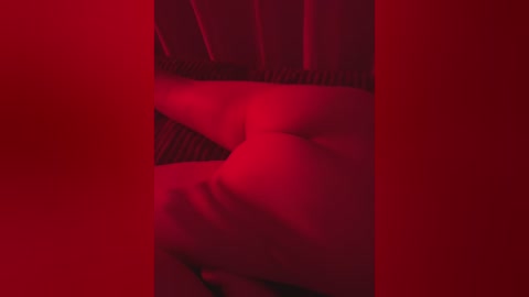 A video with a deep red hue, showing a close-up of a person's bare buttocks on a bed, with a striped pattern visible in the background.