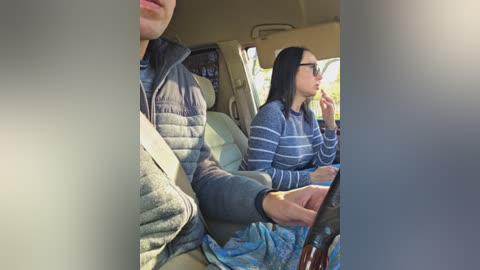 Video of an Asian woman with long black hair, wearing a blue and white striped sweater, eating a candy bar while driving in a beige car.