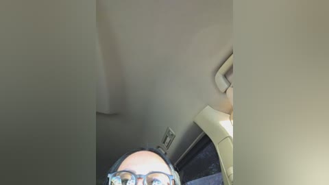 A video of a person wearing glasses and a dark jacket, peering into the car's interior from the outside, with a beige ceiling and a partially visible steering wheel.