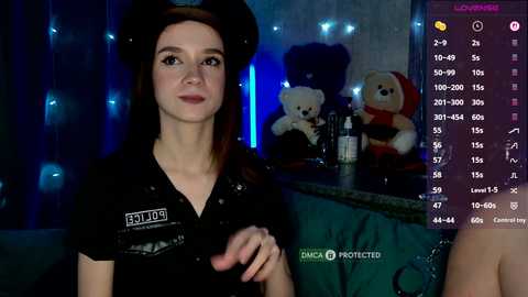 Video of a young woman in a black police uniform, holding a controller, in a dimly lit room with teddy bears.
