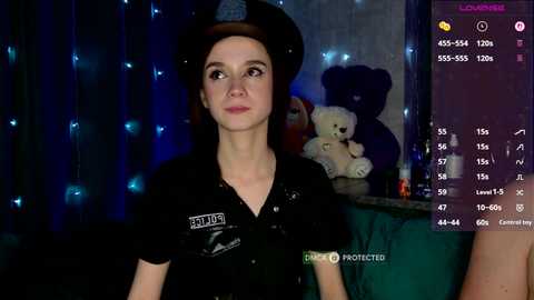 Video of a young woman with fair skin and brown hair, wearing a black uniform with a badge, standing in a dimly lit room with blue fairy lights and stuffed toys.