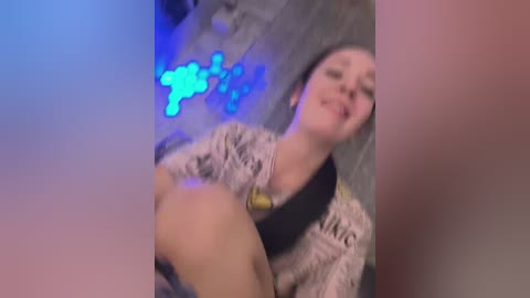 Video of a young woman with light skin and brown hair, wearing a patterned shirt, with a blue glowing symbol behind her in a dimly lit, industrial setting.