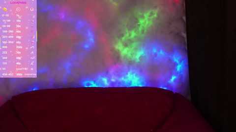 A video of a bed with a red blanket, illuminated by a vibrant, colorful LED night light emitting blue, green, and pink hues.