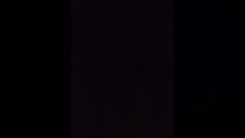 A dimly lit video shows a dark, shadowy figure standing in the center, partially obscured by the surrounding darkness. The background is mostly black, with minimal contrast, creating a sense of mystery and intrigue.