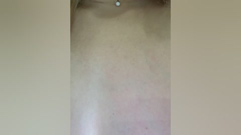 Video of a close-up view of a light-skinned person's upper chest, showcasing a small, clear navel piercing and faint redness on the skin, likely from minor irritation. The background is plain beige.