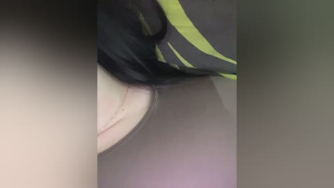 A close-up video of a person's face, partially obscured by a black and yellow striped cloth, showing a portion of their cheek and nose. The background is blurred, with muted colors suggesting an indoor setting.