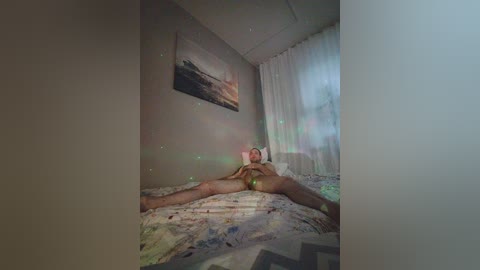 Video of a nude woman with light skin, lying on a bed with a colorful, abstract-patterned duvet, wearing a pink headband, in a dimly lit room with a painting on the wall and sheer curtains.