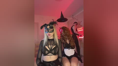 Video of two women in Halloween costumes, one wearing a black lace mask and bunny ears, the other a black witch hat.