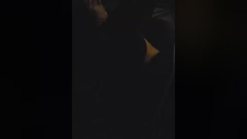 A dimly lit video of a woman in a yellow dress, standing in a dark room, her face partially obscured, creating a mysterious and eerie atmosphere.