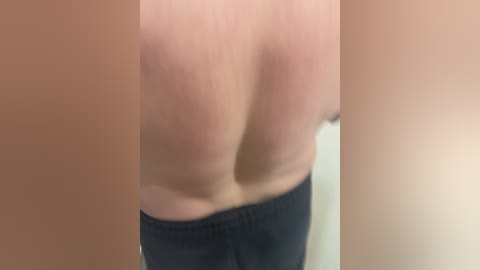 Video of a person's upper back and lower buttocks, fair skin, wearing dark pants, blurred background, emphasizing the texture and curves of the skin.