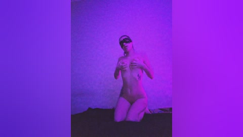 Video of a nude, light-skinned woman with medium-sized breasts, wearing a blindfold, kneeling on a dark surface in a dimly lit room with purple lighting.
