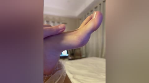 A close-up video of a person's feet, partially obscured by a door frame, in a dimly lit bedroom with beige walls and curtains. The person's toes are curled, and a television is visible in the background.