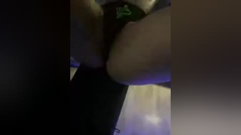 Video of a person wearing black lingerie with a green bow, standing in a dimly lit room with blurred background.