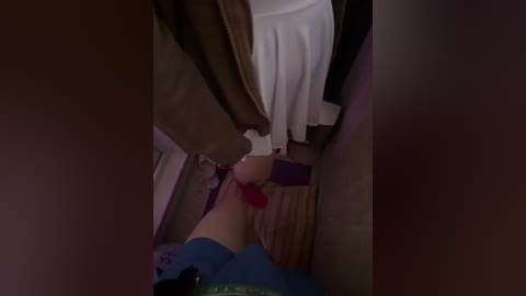 A dimly lit video of a woman in a blue shirt kneeling, wearing red panties, on a wooden floor with a bed and brown curtains in the background.