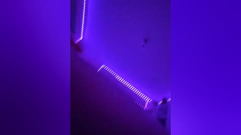 Video of a tall, narrow vertical structure bathed in vibrant purple light, featuring a zigzag pattern of white light strips, creating a dynamic, futuristic atmosphere.