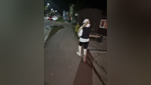 Video of a woman walking on a suburban street at night, wearing a white hat, black jacket, and shorts, with a flashlight in her right hand. Streetlights and cars are visible in the background.
