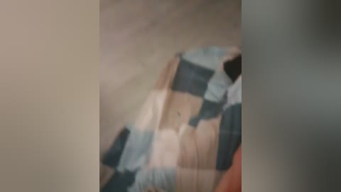 A blurred video of a woman in a blue and white checkered shirt lying on a bed, with a beige wall in the background.