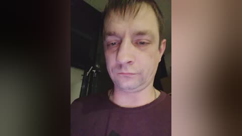 Video of a man with pale skin and short brown hair, wearing a dark shirt, indoors, blurred background.