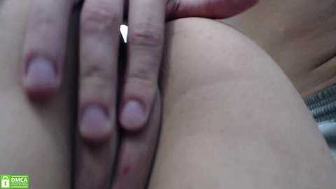 A close-up video of a fair-skinned person's hand gently grasping a smooth, pale buttock, with a green logo in the lower left corner.
