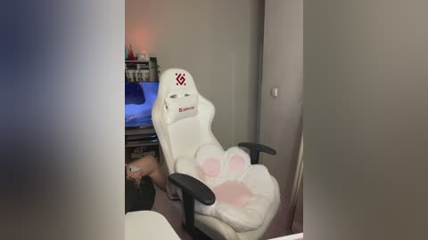 Video of a gaming setup with a white Razer gaming chair, a flat-screen TV showing a blue screen, and a shelf holding gaming accessories.