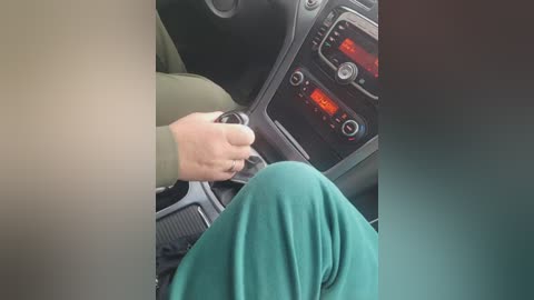 Video of a hand turning a car key in the ignition, displaying a dashboard with a red digital display. The person is dressed in a green shirt.