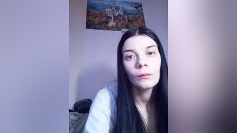 Video of a young woman with long black hair, wearing a white shirt, standing in a dimly lit room with a painting of a medieval castle on the wall.