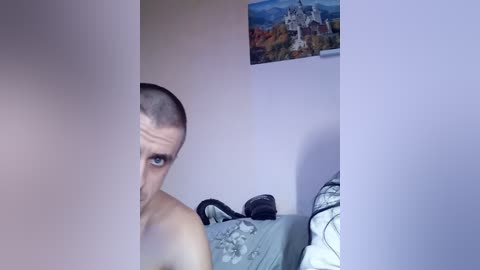 Video of a young, shirtless man with short hair, peering through a partially closed door into a dimly lit bedroom with a bed, a poster of a castle on the wall, and scattered clothes.