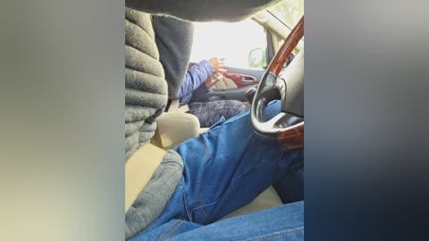 Video of a person wearing a gray jacket, blue jeans, and beige shoes sleeping in the back seat of a car.
