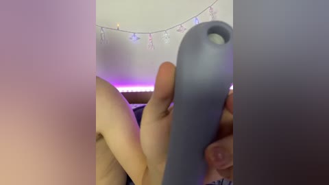 A video of a person using a gray Nintendo Switch controller, holding it near their face, in a dimly lit room with a string of fairy lights in the background.