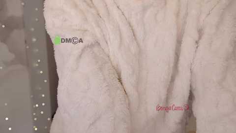 Video of a plush, cream-colored bathrobe with \"DMCA\" and \"lemoncandy\" logos, featuring soft, fuzzy texture.